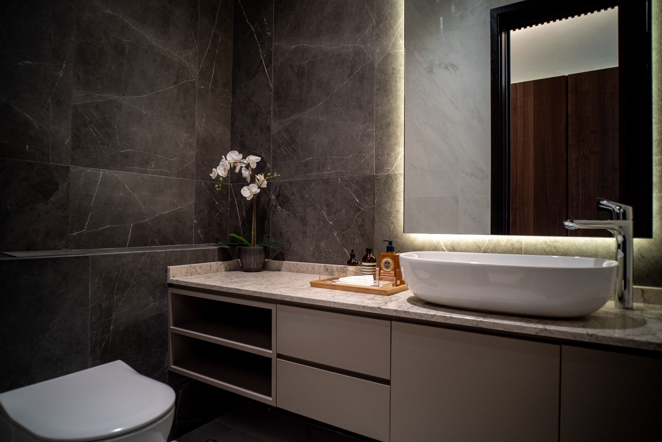 Dark modern luxury interior design for marble toilet with custom shelves and vanity mirror and overcount sink